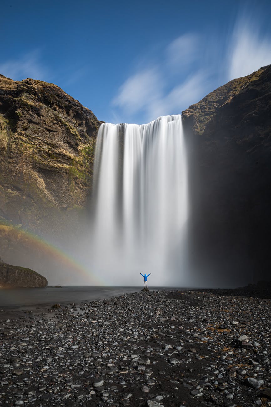 unrecognizable traveler between rainbow and waterfall